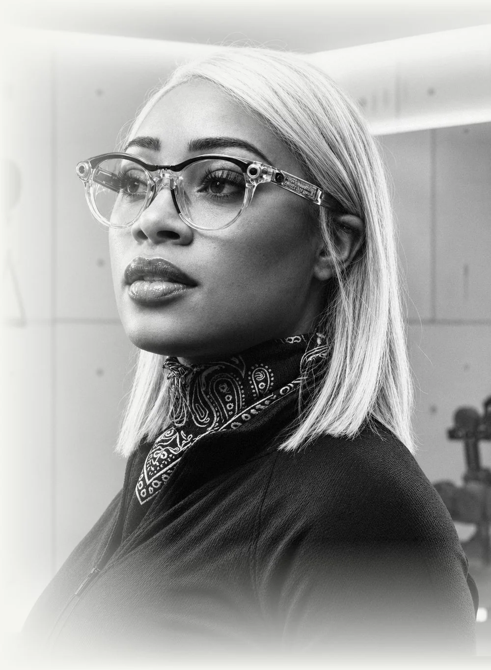 Dice Gamble, platinum hair and clear-frame glasses, in a bright studio